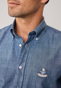 Lichtblauwe denim overhemd met knopen, voorzien van een puntige kraag, borduursel op de borst en witte plastic knopen, gemaakt van een zachte, gestructureerde stof.