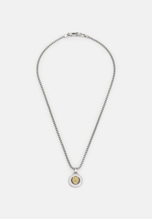 Colar em corrente de tom prateado com um pendente redondo que apresenta um emblema de leão dourado, borda detalhada e fecho.