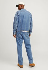 Casaco de ganga azul claro com um corte descontraído, vista traseira exibindo uma bainha crua e costuras em contraste, combinado com jeans soltos a condizer e botas castanhas.