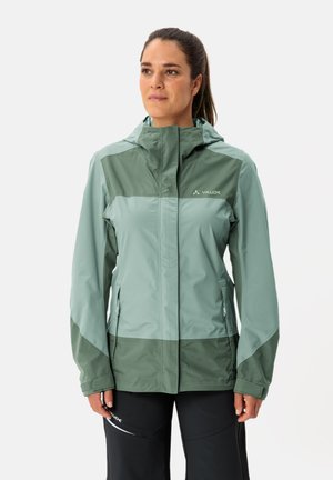Veste imperméable en vert clair et foncé, avec une capuche, des poches zippées et une texture lisse. Le design comprend des éléments de blocage de couleurs.