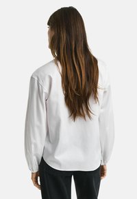 Long-sleeve white blouse with a relaxed fit, featuring elastic cuffs and a smooth texture. Worn with dark jeans, showing a simple design.