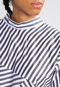 Gros plan sur des lèvres et un cou avec des cheveux tressés portant un vêtement à rayures verticales noir et blanc à col haut.