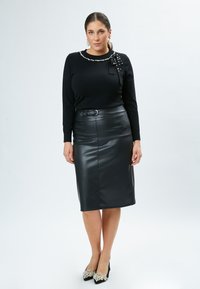 Schwarzer Strickpullover mit Perlenbesatz und Schleifendetail, kombiniert mit einem hoch taillierten schwarzen Bleistiftrock aus Kunstleder und verzierten schwarzen Pumps.