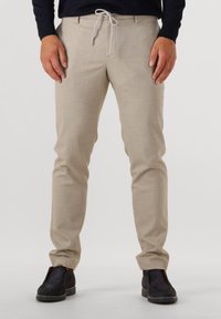 Beige trousers with a textured finish, featuring a drawstring waist and slim fit. Paired with black slip-on shoes.