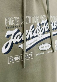 Sweat à capuche kaki avec des inscriptions blanches et bleu marine comprenant "Jack & Jones", "Fine Cotton Selection", "Denim Legacy" et les noms des villes Barcelone et Copenhague.