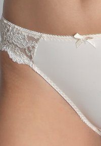 Białe bielizna z koronkowymi wykończeniami i akcentem w postaci kokardy. Gładki materiał z teksturowaną koronką po bokach i falbaniastymi detalami wzdłuż krawędzi.