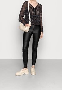 Svart mönstrad genomskinlig blus med långa ärmar, ihop med svarta fusk läder leggings och beigefärgade klumpiga loafers, samt en liten beigemelerad axelväska.