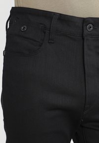 Černé džíny z denimu s přiléhavým střihem. Obsahují přední kapsy, poutka na opasek a zapínání na knoflík. Hladká textura, minimální švy.