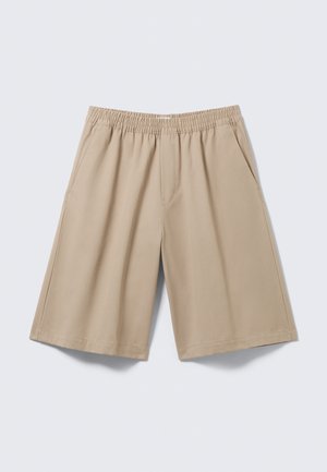 Shorts beige longueur genou avec taille élastique et poches latérales, posés à plat sur un fond gris clair.