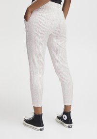 Witte broek met een roze verticale streepprint, elastische tailleband en zijzakken, gedragen met zwarte hoge sneakers.