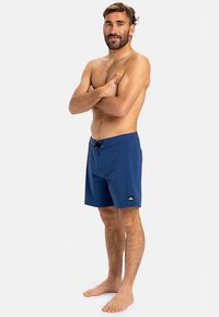 Tumesinised ujumispüksid, mis on valmistatud kergest materjalist, varustatud elastse vöökohaga ja nöörkinnitusega ning väikese logoplaastriga.