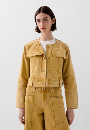 Cropped yellow denim jacket with two front flap pockets, button closure, and a slightly textured finish. Worn over a white top.