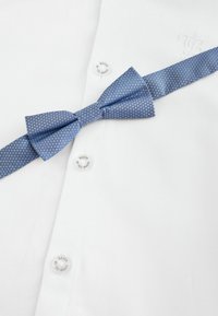 Weißes, strukturiertes Hemd mit einem blauen gepunkteten Fliegen, Logo-Knöpfen und glattem Stoff. Die Fliege ist mittig platziert und liegt auf dem Kragen.