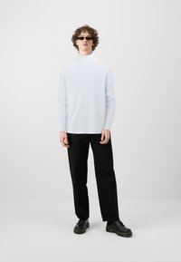 Fehér, hosszú ujjú, garbós póló, fekete, bő szárú nadrággal és fekete cipővel párosítva. Kiegészítők között sötét napszemüveg szerepel. Egyszerű, modern dizájn.