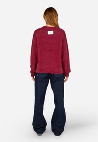 Sweater felpudo cor de vinho com um decote redondo e um etiqueta na parte de trás, combinado com jeans flare azul escuro com bolsos laterais e costuras simples.