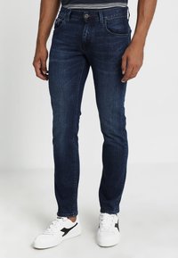 Jeans blu in denim a taglio aderente con finitura sbiadita, design a cinque tasche e chiusura con bottoni. Abbinati a sneakers bianche con dettagli neri.