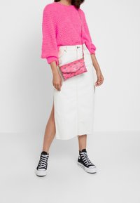 Pull en tricot rose vif à manches longues, jupe midi en denim blanc avec une fente sur le côté, et baskets montantes noires. Petit sac à main rose à motifs.