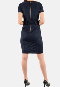 Laivansinis farkkupuku lyhyillä hihoilla, vartalonmyötäinen malli, näkyvät ompelutiedot, takana vetoketju ja vyötäröllä vyö. Yhdistetty mustiin korkokenkiin.