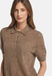 Brun stickad polo med korta ärmar, med ett strukturerat diamantmönster och detaljer med tre knappar vid kragen.