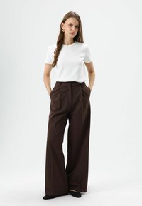 T-shirt blanc à manches courtes associé à un pantalon large marron taille haute. Le vêtement présente une texture lisse et des lignes épurées et modernes.