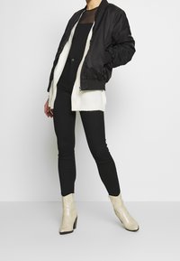 Svart bomberjacka med vit fleecelinning, lager på en svart topp och parat med svarta skinny jeans och beige klackstövlar med ormskinnsmönster.