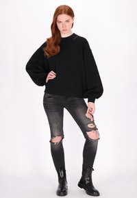 Czarny sweter z oversize'owymi rękawami i okrągłym dekoltem, zestawiony z przetartymi czarnymi wąskimi dżinsami z dziurami na kolanach oraz czarnymi botkami za kostkę.
