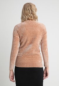 Lange mouwen pullover trui in een zachte perzikkleur, met een gestructureerde brei en geribbelde onderkant. De achterkant toont een losse pasvorm en lichtgewicht ontwerp.