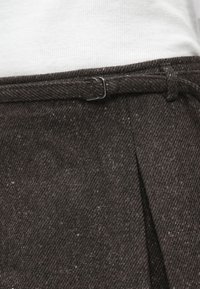 Brown textured fabric with a subtle pattern, featuring a belt loop and a metal buckle, part of a tailored garment's waist area.