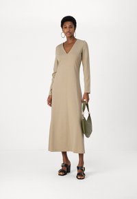 Beige pika-skilee dress silehhi madala V-kaelusega. Omab sirget siluetti ning on kombinatsioonis paksude mustade sandaalide ja rohelise kotiga.