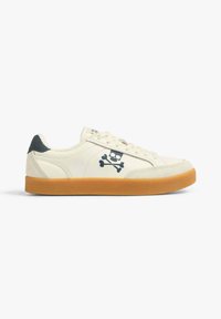 La chaussure présente un dessus en cuir crème, une semelle extérieure en caoutchouc gomme, des accents bleu foncé et un imprimé de crâne et os croisés. Design classique de sneaker.