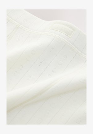 Tela blanca de punto con textura acanalada, que presenta pequeños patrones de diamante y una etiqueta con "NEXT" cerca del borde superior.