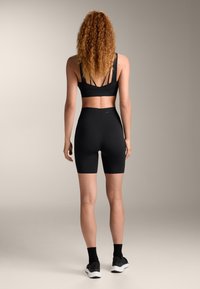 Čierny športový crop top s tenkými ramienkami a čiernymi šortkami s vysokým pásom. Mäkka tkanina s hladkou textúrou, vhodná na cvičenie.