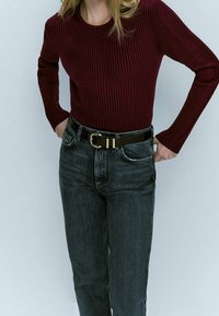 Burgundowy prążkowany top z długim rękawem w połączeniu z jeansami z ciemnego denimu z wysokim stanem. Ubranie uzupełnia czarny pasek z złotą klamrą.