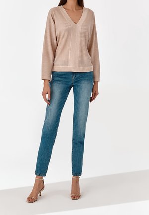 Beige ribbed sweater with V-neck, paired with light blue straight-leg jeans and beige heeled sandals, featuring a smooth texture and minimalist design.
