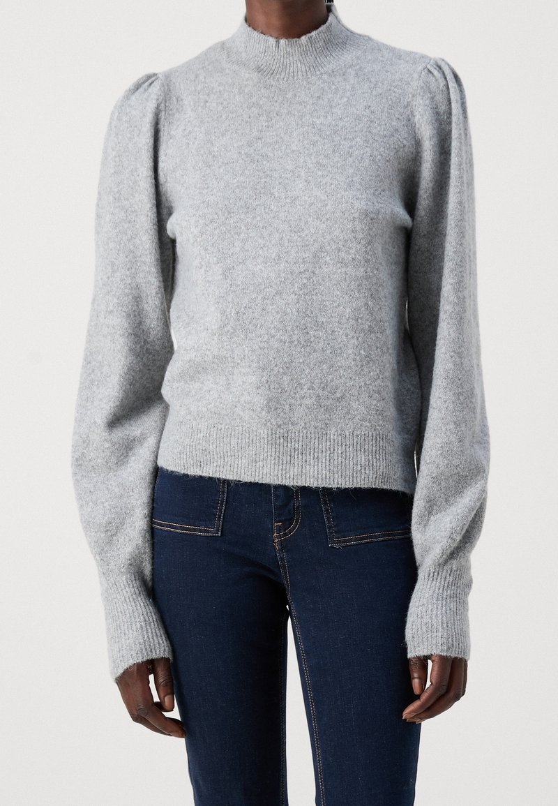 Personne portant un pull en tricot gris clair à manches longues avec un col rond et un jean bleu foncé ajusté.