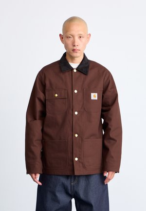Veste en toile brune avec un col en velours côtelé noir, dotée de boutons dorés et de deux poches avant. Le matériau a une texture durable.