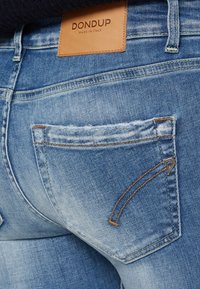 Světle modré džíny s vybledlým vzhledem, s hnědou koženou etiketou a podrobným prošíváním na zadní kapse.