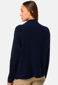 Pull marin à côtes avec col montant et épaules tombantes, offrant une texture douce et une coupe décontractée dans le dos.