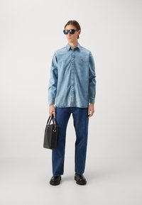 Denim shirt in light blue, buttoned, with collar; dark blue jeans; worn with black sunglasses and a textured black handbag; smooth footwear.