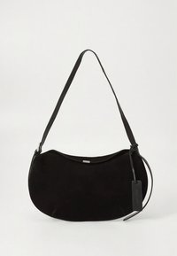 Svart mockaväska med kurvad form, enkel axelrem och en dekorativ etikett. Mjuk textur med minimala beslag och utan synliga mönster.