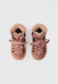Botas de couro cor-de-rosa com um colarinho em imitação de pêlo, cadarços texturizados e acessórios metálicos. Solas de borracha com detalhes de costura visíveis.