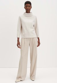 Lichtgrijze, gebreide trui met een hoge, geribbelde kraag en een gestikte voorpaneel, gecombineerd met beige, wijde broek en zachte, low-profile schoenen.