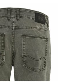 Harmaat farkut, joissa on teksturoitu pinta, musta etiketti vyötäröllä ja kaksi takataskua, joissa kaarevat ompelukoristeet.