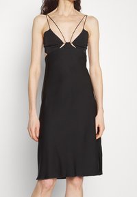 Černé bezramínkové šaty s tenkými špagetovými ramínky, vyznačující se hlubokým V-výstřihem a výřezy na bocích, vyrobené z hladkého materiálu.