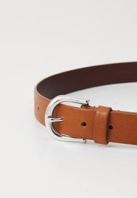 Brun lærbelte med en glitrende sølvspenne, med hull for justering og en jevn tekstur. Enkel, klassisk design.