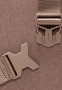 Tessuto marrone chiaro con una superficie texture, caratterizzato da clip di plastica in una tonalità più scura, una delle quali ha una forma e un design unici.