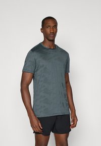 T-shirt σε σκούρο πράσινο καμουφλάζ από ελαφρύ ύφασμα, με στρογγυλή λαιμόκοψη και κοντά μανίκια, σε συνδυασμό με μαύρες σορτς.