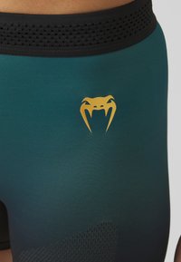 Shorts de sport teal avec une ceinture texturée noire. Présente un logo serpent doré sur le devant et un accent en mesh sur le côté.