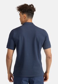 Námorně modré polo tričko s krátkým rukávem a límečkem. Tkanina vypadá hladce a má standardní střih se bočními rozparky na lemu.