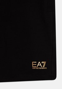 Melni sporta šorti, izgatavoti no kokvilnas maisījuma, piedāvā zelta EA7 Emporio Armani logo apakšmalā un gludu tekstūru bez redzamām rakstām. 